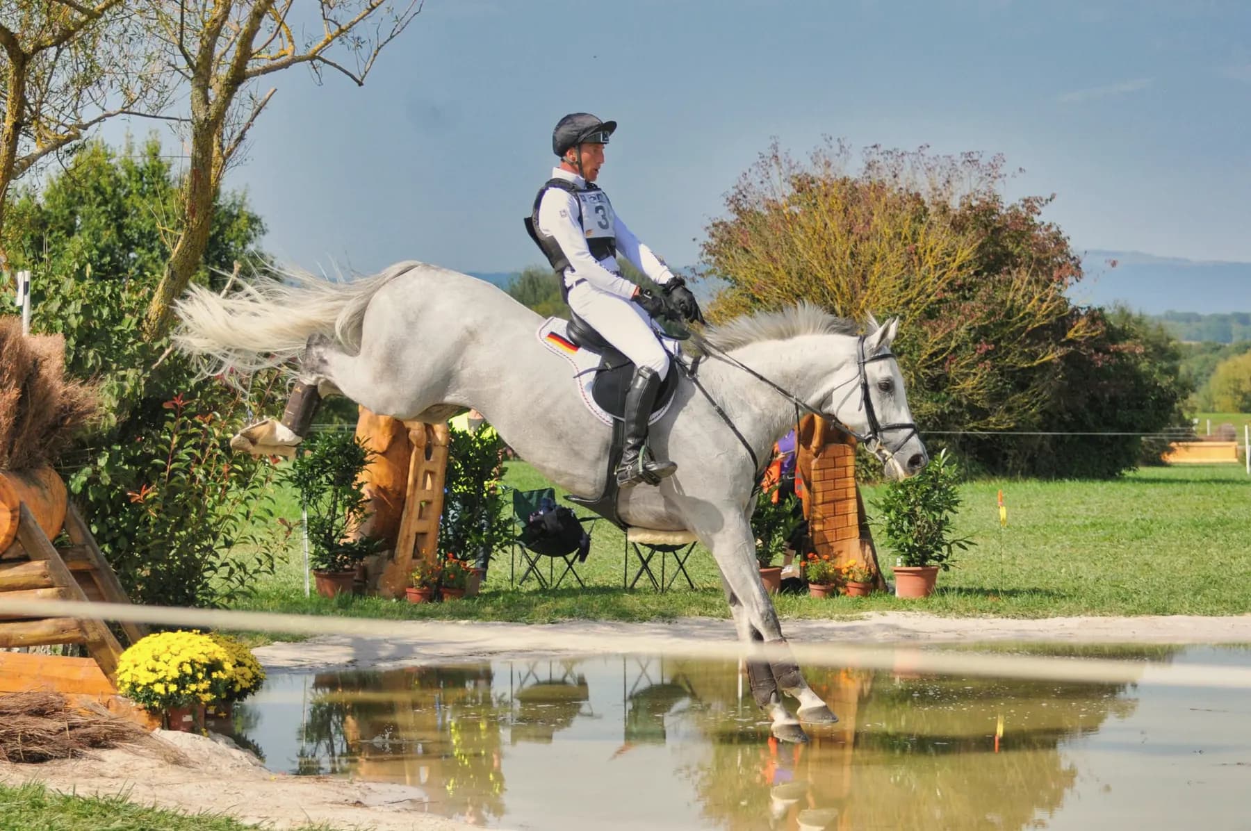 Ruiter met bodyprotector en cap springt met een paard over een crosshindernis