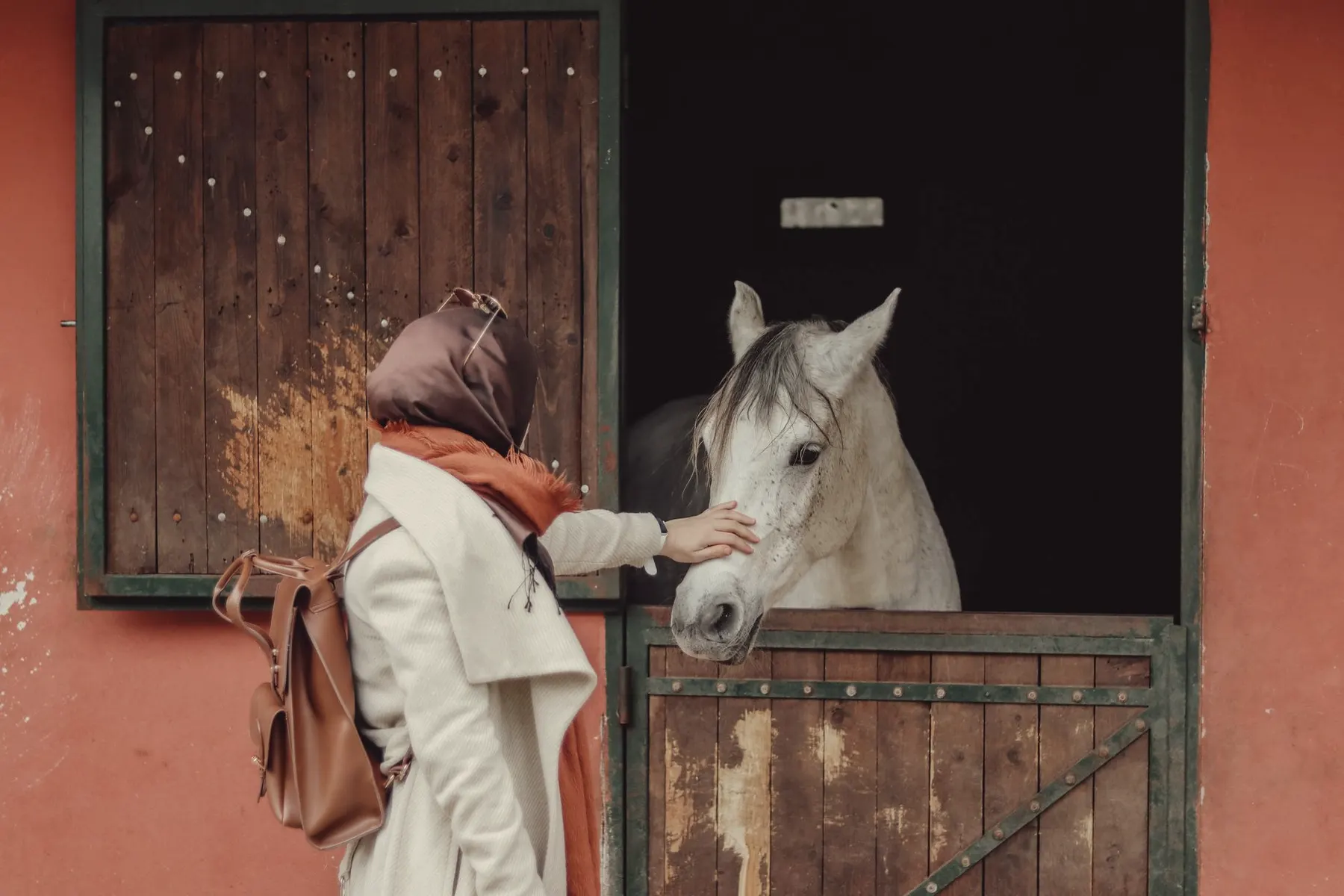 Ruiter staat bij de staldeur met haar paard